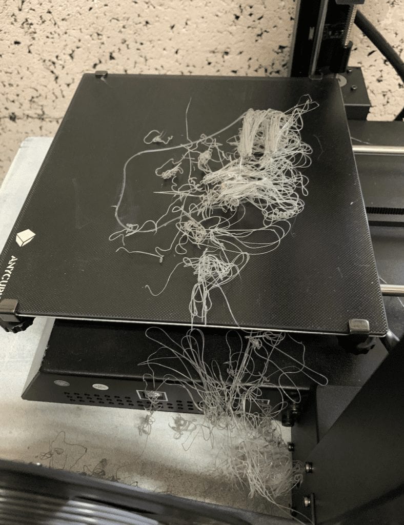 Photo of 3D printing machine with gray filament strewn about.